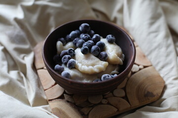 Sweet dumplings (vareniki) topped with frozen blueberries, served in a rustic wooden bowl. The cozy winter setting emphasizes warmth and comfort, making it perfect for food photography or traditional 