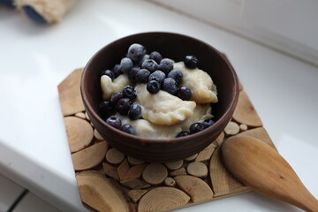 Sweet dumplings (vareniki) topped with frozen blueberries, served in a rustic wooden bowl. The cozy winter setting emphasizes warmth and comfort, making it perfect for food photography or traditional 