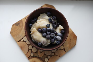Sweet dumplings (vareniki) topped with frozen blueberries, served in a rustic wooden bowl. The cozy winter setting emphasizes warmth and comfort, making it perfect for food photography or traditional 
