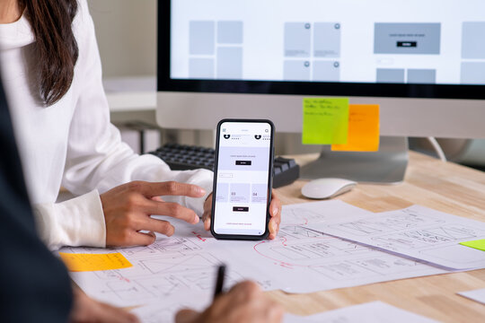 UX UI designer testing prototype on a phone, discussing and brainstorming on wireframes for a website and mobile app prototype, in the concept of website and mobile application design concept.	