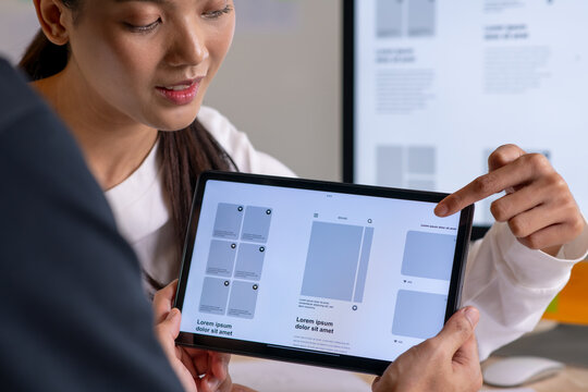 UX UI designer testing prototype on a tablet, discussing and brainstorming on wireframes for a website and mobile app prototype, in the concept of website and mobile application design concept.