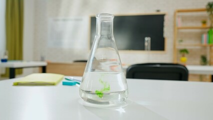 Empty school chemistry classroom with desks, chairs and chalkboard, workspace for teaching and studying. Glass bottle with green ink in liquid on table.