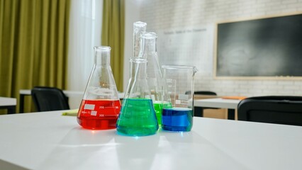 Empty school chemistry classroom with desks, chairs and chalkboard, workspace for teaching and studying. Glass bottles with colorful liquids close up.