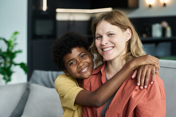 Smiling woman being hugged by child with bright expression while sitting on a couch in a modern living room setting