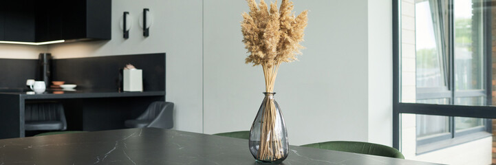 Vase filled with dried pampas grass positioned on dark marble countertop in sleek modern kitchen with minimalist design and large windows for natural light