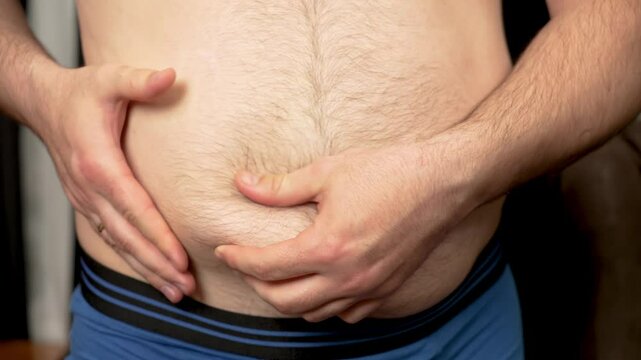 Man pinching fat fold on stomach close up. unrecognizable Male squeezing fat roll on belly. Guy gripping fat fold on abdomen