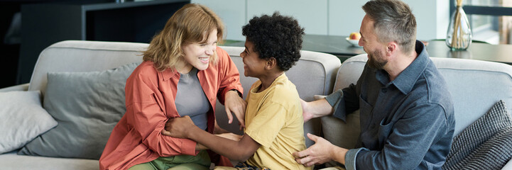 Multiracial family sitting on couch, laughing and enjoying each other's company. Warm interaction...