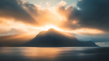 Sunset rays illuminating a mountain peak near the shoreline with a calm sea in the foreground