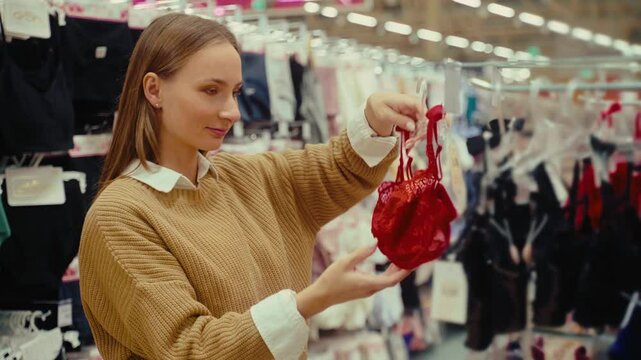 A woman browses through a selection of bras in a well-lit store, carefully examining each option before making her choice. Her thoughtful process shows the importance of finding the right fit.