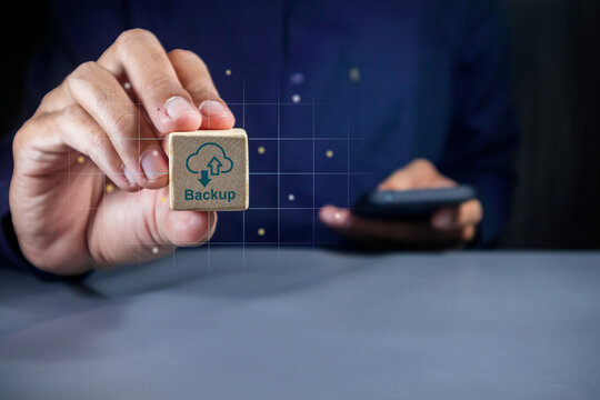 Man holding a smartphone and a wooden block with Backup symbol. Phone data backup and cloud data storage concept.
