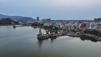 Naklejka premium Aerial view of Kaohsiung serene waterfront with cityscape and green hills in twilight