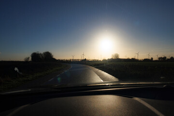 Obraz premium Driving through low sunlight on a wet road with wind turbines in the background during early morning hours