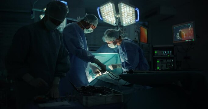 Medical Team Performing a Complex Surgery on a Patient, Using Specialized Tools, Looking at Digital Screens with Health Information. Doctors with a Female Surgeon in the Lead Saving Patient's Life