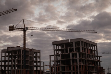 Silhouettes of construction cranes against sky with dark clouds