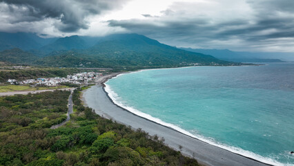 Breathtaking coastal view of Taiwan showcasing waves meeting dark sandy beach and lush greenery