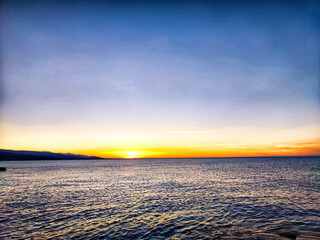 Naklejka premium Sunset over the tranquil ocean at a coastal location with soft colors painting the sky and water in the early evening