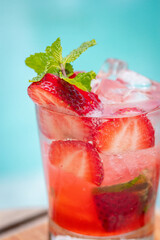 Close up view, Strawberry mojito in a glass with slice strawberries, mint leaves on a wooden surface near a pool
