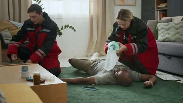 Emergency paramedics assisting unconscious Black man with diabetes lying on floor after severe hypoglycemia, preparing injection and using bag valve mask for respiratory support at home