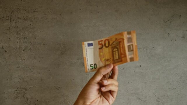 Hand holding fifty euro banknote against concrete background, showcasing european currency in a minimalist setting