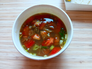 Close up of Soto Ayam Medan or Indonesian style chicken soup in white kraft paper bowl isolated on wooden background.