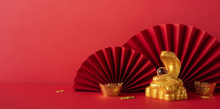 A vibrant red and gold themed setup showcasing traditional Chinese new year decorations, including a gold snake statue symbolizing the year 2025, complemented by red paper fans