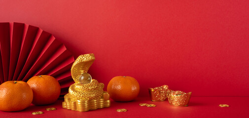 Festive Chinese New Year 2025 setup with a golden snake, tangerines, and oriental decorations on a red background symbolizing good fortune and tradition