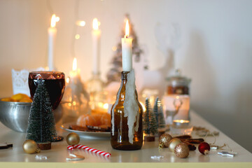 Various Christmas decorations, cookies, chocolate, nuts and tangerines, wine glasses and lit candles on the table. Holiday hygge at home. Selective focus.