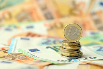 One euro coin lies on huge amount of different euro dollars banknotes