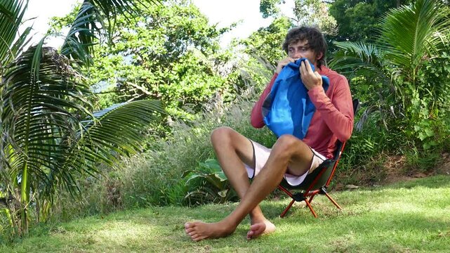 a man inflates a camping and trekking ultralight pillow with his mouth, inflation process, in a forest with a tropical background