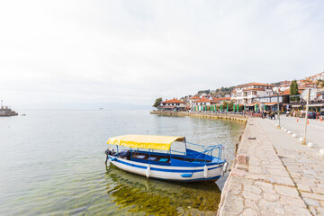 Obraz premium Traditional boat in the waters of Lake Ohrid with colorful houses lining the shore.