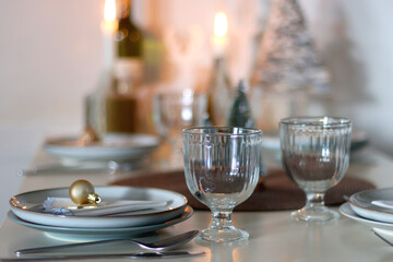 Table set for Christmas meal with plates, glasses, holiday decorations, lit candles and wine. Selective focus.