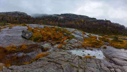 A rocky landscape with patches of grass and small puddles under a cloudy sky.