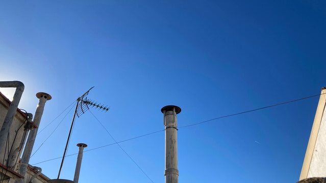 Vista contrapicada de antena de televisi&oacute;n y chimeneas de viviendas con cielo azul al fondo