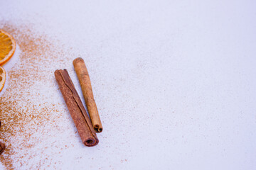 A pile of orange slices and cinnamon sticks on a white background. The oranges are cut in half and the cinnamon sticks are whole. Concept of warmth and comfort