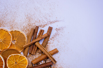 A pile of orange slices and cinnamon sticks on a white background. The oranges are cut in half and the cinnamon sticks are whole. Concept of warmth and comfort