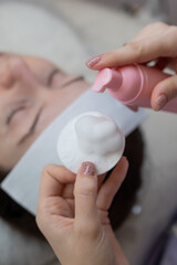 A professional applies cleansing foam to a cotton pad in a beauty salon. 