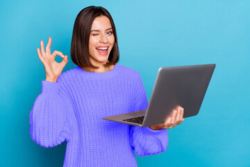 Portrait of attractive cheerful skilled girl using laptop showing ok-sign winking isolated over bright blue color background