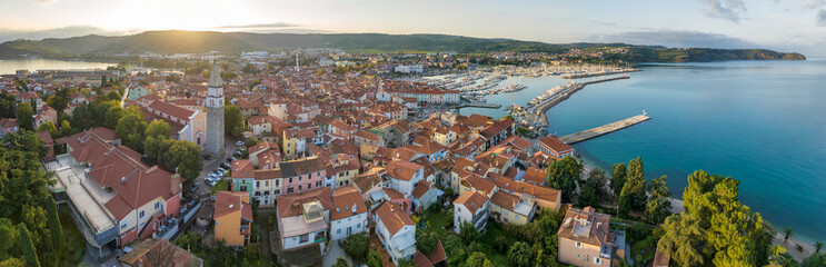 Fototapeta premium Aerial panoramic view of picturesque Izola town with the old town and buildings with red roofs, the main promenade, the marina with boats on Adriatic sea coast, Slovenia.