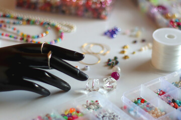 Hand figurine, colorful friendship bracelets, necklaces, various beads and DIY supplies on the table. Making jewelry at home. Selective focus.