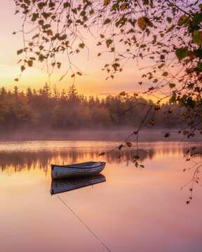 Lone boat floating on Loch Rusky at sunrise, Highlands, Scotland, United Kingdom