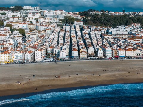 The lively beach, revealing rows of charming houses with red roofs and people enjoying the sandy shore under a clear sky, Nazare, Oeste, Estremadura, Portugal