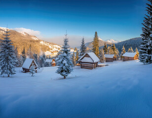 Naklejka premium A picturesque winter landscape shows snow-covered cabins nestled among evergreen trees with mountains in the background against a bright blue sky.