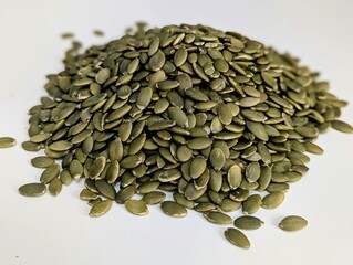A close-up of a small pile of pumpkin seeds spread out on a pristine white surface, showcasing their natural texture and earthy green hues. These seeds are packed with nutrients, including zinc
