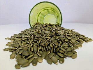 A close-up of a small pile of pumpkin seeds spread out on a pristine white surface, showcasing their natural texture and earthy green hues. These seeds are packed with nutrients, including zinc