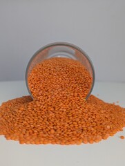 A close-up shot of vibrant orange lentils spread across a clean white surface, showcasing their...