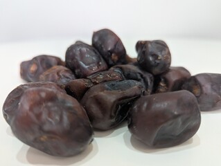 Close-up of fresh dates arranged on a white table, emphasizing their natural texture and rich brown hue. The photo highlights the glossy, plump fruits, renowned for their sweet taste \