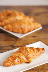Artisan croissant handmade in a bakery. Close-up of croissant on a rectangular white plate. Continental breakfast, to be filled with sweet or savory ingredients.