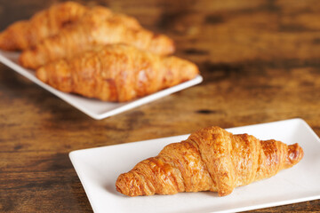 Artisan croissant handmade in a bakery. Close-up of croissant on a rectangular white plate. Continental breakfast, to be filled with sweet or savory ingredients.