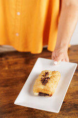 Close-up of a woman's hands holding a plate with a freshly baked chocolate neapolitan. The clerk serves a handmade neapolitan in the cafe. Sweet or savory breakfasts or snacks.