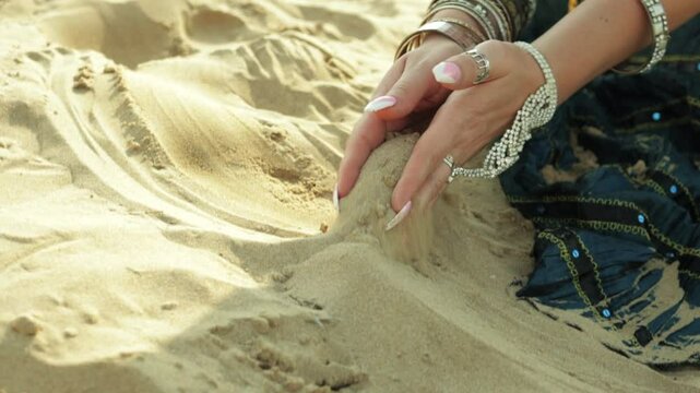 Woman in Belly Dancer Outfit Gracefully Lets Sand Fall From Hands in Stunning Desert Setting, Showcasing Beauty and Sensuality of her Movement and Traditional Attire